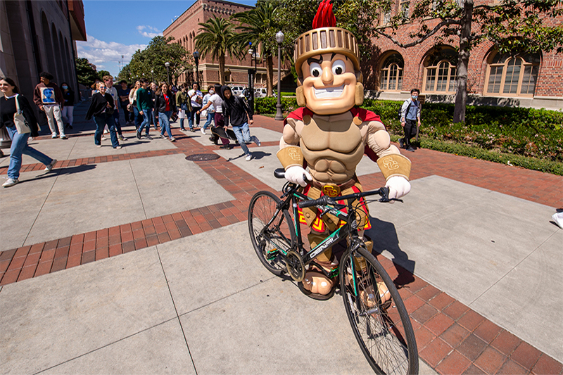 Tommy Trojan rides a bike to campus
