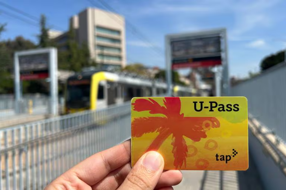 A person holding a U-Pass card in front of a rail line.