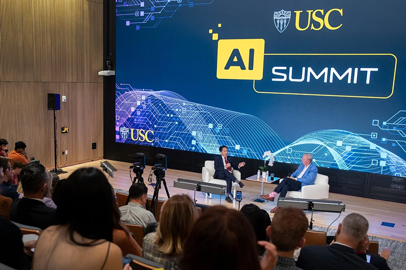 Speakers participate in an onstage discussion at the USC AI Summit in front of a large screen displaying the event title.